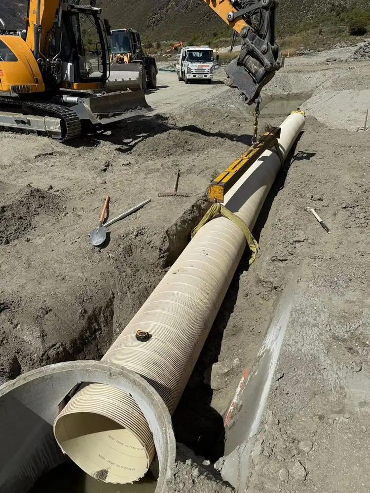 Excavator lowering a ribbed pipe liner into a concrete pipe in an open trench