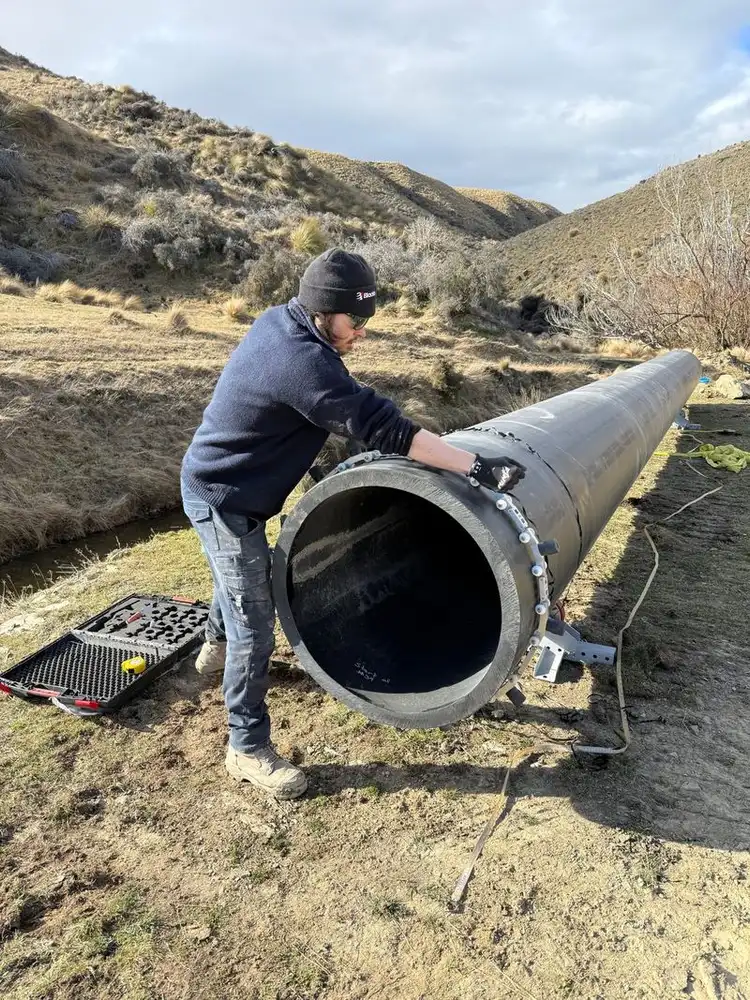 Worker lining up a large black polyethylene pipe beside a stream in tussock hills