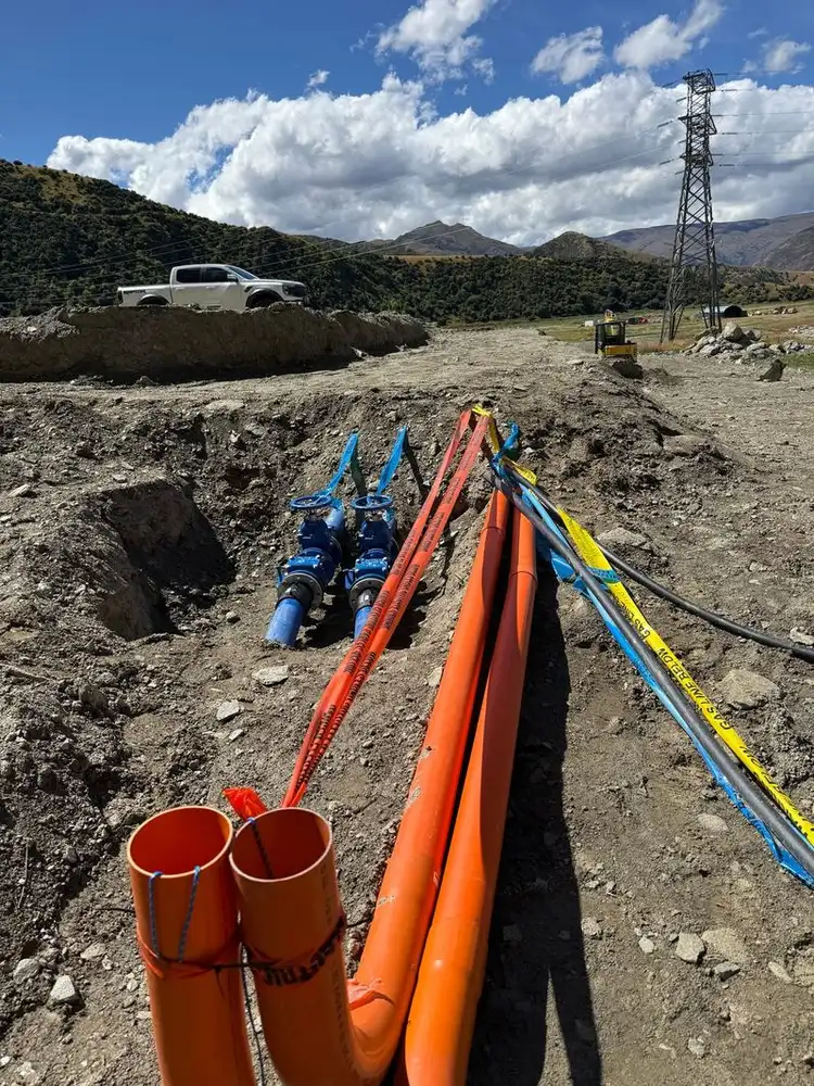 Blue gate valves and orange ducts laid in a trench on a hillside site