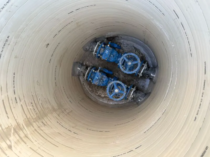 Looking down a lined chamber at two blue gate valves on the pipework